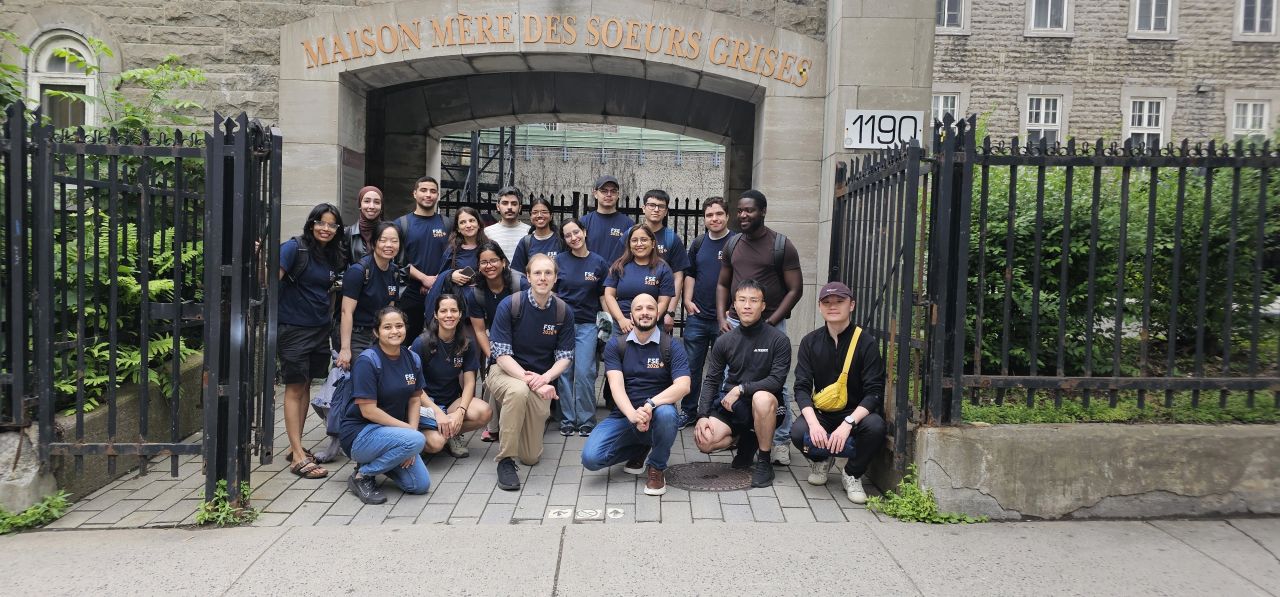 Around twenty FSE 2026 student volunteers in navy conference shirts, posing in front of the arched gate of the Maison mère des Sœurs Grises on Concordia's campus in Montréal.