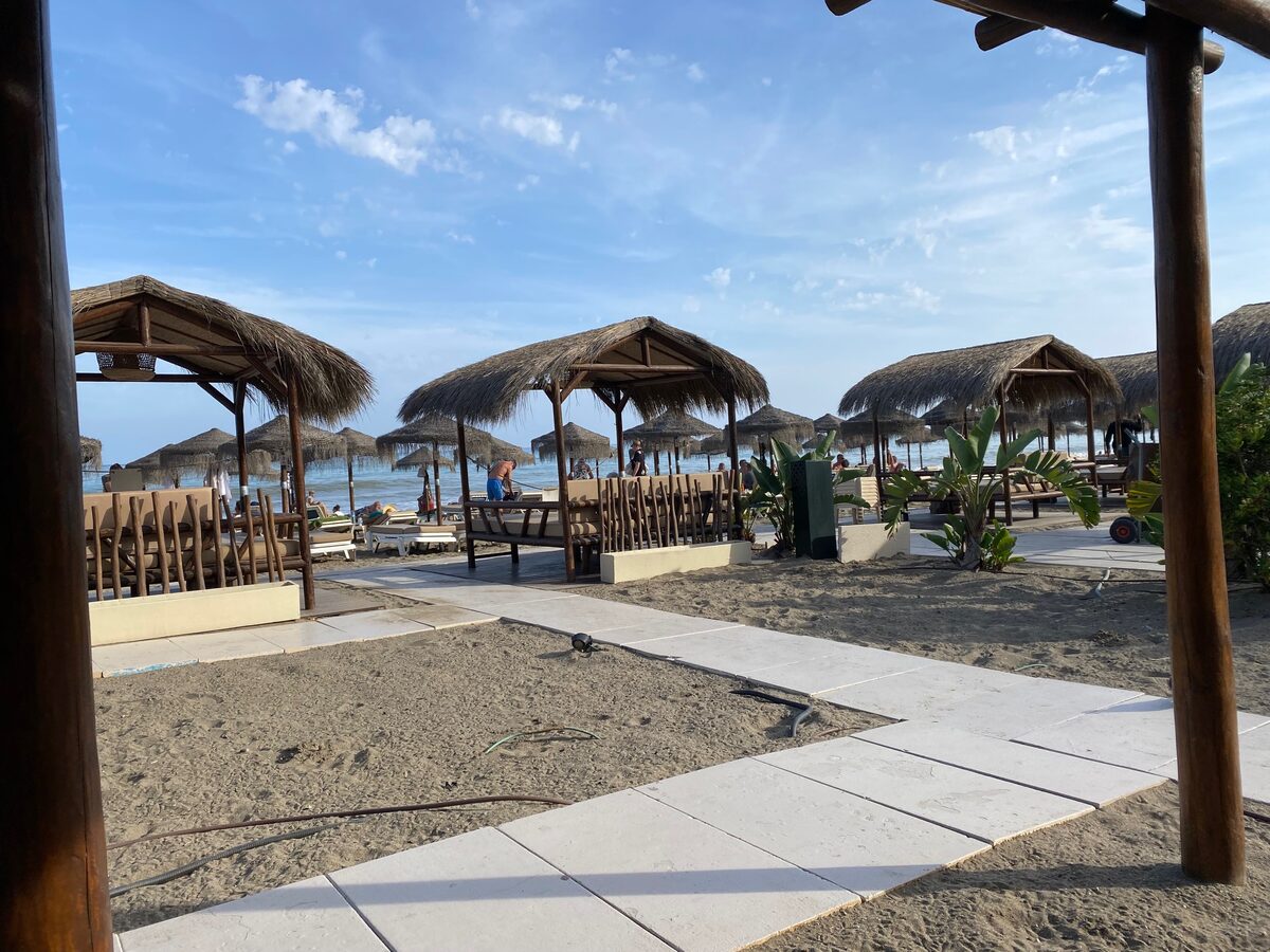 Thatched sun shelters and wooden lounge chairs on the sand, with the sea behind them, at the beach in front of the conference hotel in Málaga.